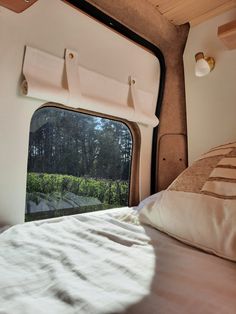 there is a bed with white sheets and pillows in front of a window that looks out onto the woods