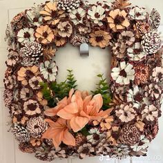 a wreath with flowers and pine cones hanging on a door