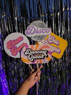 someone holding up some paper signs in front of purple and blue tinsel