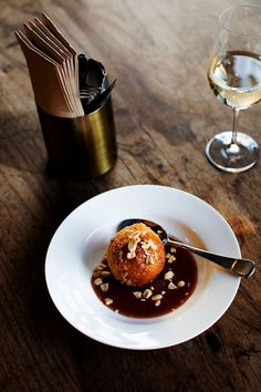 a white plate topped with food on top of a wooden table next to a glass of wine