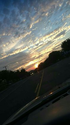 the sun is setting behind some clouds in the sky over a street with cars driving down it