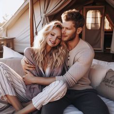 a man and woman sitting on top of a bed next to each other in front of a tent