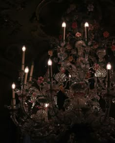 a chandelier with many candles lit up in the dark, surrounded by flowers and leaves