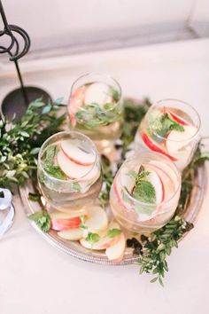 four glasses filled with water and fruit on top of a table next to greenery