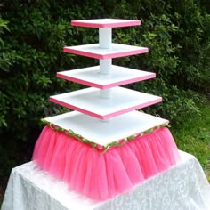 three tiered cake stand with pink and white tulle skirt on table in front of bushes