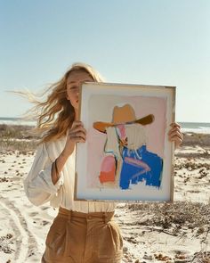 a woman holding up a painting on the beach