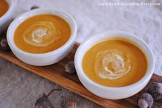 three white bowls filled with soup sitting on top of a wooden tray next to nuts