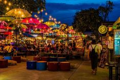 people are walking through an outdoor market with umbrellas and lights hanging above them at night