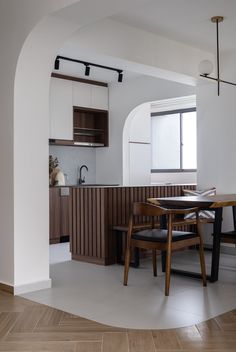 an open kitchen and dining room area with wood flooring, white walls and cabinets