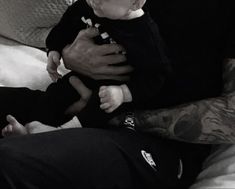 a man holding a baby in his arms while sitting on a couch with a tattoo on it's arm