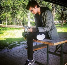 a young man sitting on top of a wooden table next to a park bench while looking at his cell phone