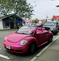 a pink car is parked on the side of the road in front of some cars