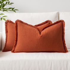 two orange pillows sitting on top of a white couch next to a potted plant