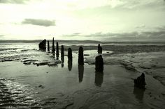 an old wooden post sticking out of the water on a beach at low tide with clouds in the background