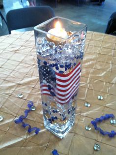 an american flag candle sits in a glass vase filled with water and confetti