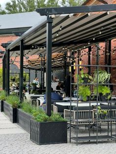 an outdoor dining area with tables, chairs and potted plants on the side walk