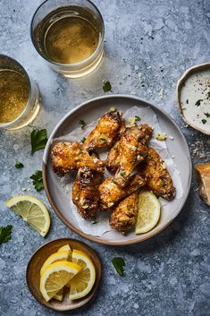 chicken wings with lemons and herbs on a plate next to two glasses of beer