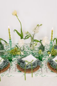 the table is set with green and white plates, napkins, flowers and candles