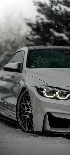 a white car parked on the side of a road in front of snow covered trees