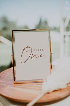 a table sign sitting on top of a wooden table next to a white feather ornament