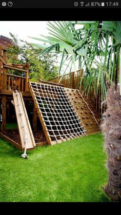 a wooden slide set in the grass next to a palm tree and a large potted plant