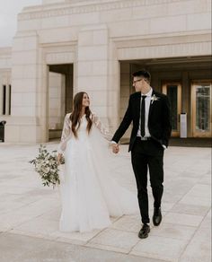 a bride and groom holding hands walking in front of a building