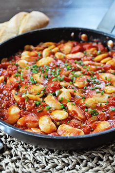 a skillet filled with pasta and sauce on top of a woven place mat next to bread