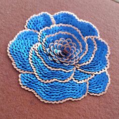 a blue flower made out of plastic beads sitting on the ground next to a wall