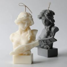 two small candles are next to each other on a white surface, one is holding a guitar and the other has a statue