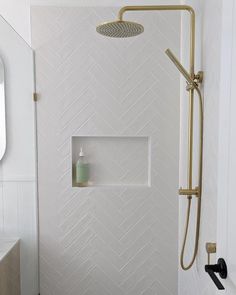 a bathroom with white tile and gold shower faucet next to a mirror on the wall