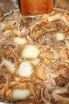 mushrooms and onions cooking in oil in a pan on the stove top with a wooden spatula