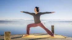 a woman practices yoga on a dock by the water