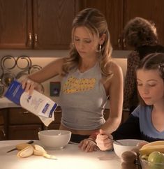 two women are in the kitchen preparing some food and one is pouring something into a bowl