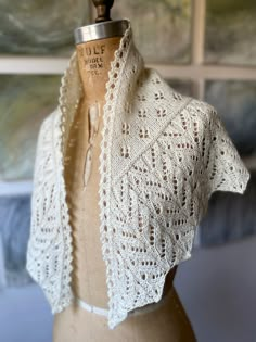 a mannequin wearing a white crochet shawl on top of a dress form