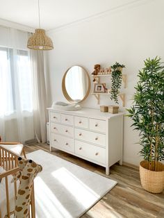 a baby's room with a dresser, mirror and potted plant