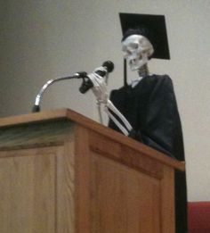 a skeleton wearing a graduation cap stands at a podium