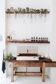 a wooden table topped with lots of bottles next to a shelf filled with plants and candles