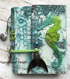 an altered book with green and blue designs on the cover, featuring a seahorse