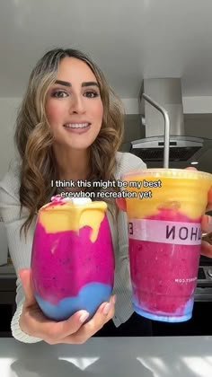 a woman holding two cups with different colored drinks in them