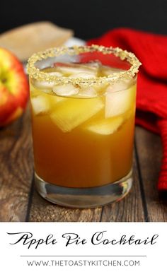 an apple cider sits on a wooden table next to some apples and a red towel