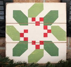 a wooden block with green and red designs on it sitting in front of a brick wall