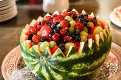 a watermelon bowl filled with grapes, cherries and other fruit sits on a plate