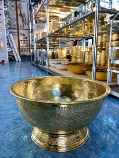 a large metal bowl sitting on top of a blue tile floor next to shelves filled with gold dishes