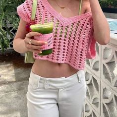 a woman in white pants and a pink top holding a green smoothie up to her face