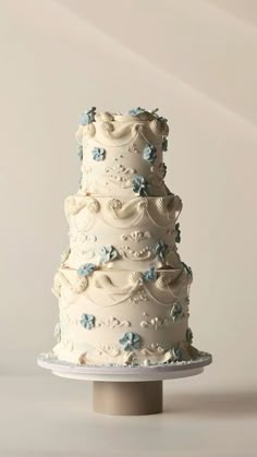 a three tiered wedding cake with blue flowers on the top and bottom, sitting on a pedestal