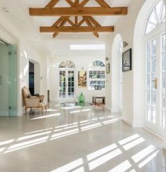 the sun shines through two arched windows in an open floor plan with white walls and wood beams