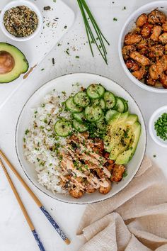 a white plate topped with rice, cucumber and chicken next to bowls of vegetables