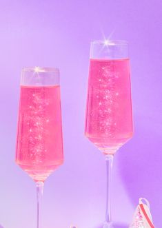 two wine glasses filled with pink liquid next to candy canes on a purple background