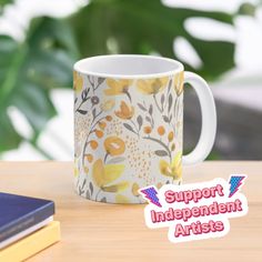 a coffee mug sitting on top of a wooden table next to a book and plant