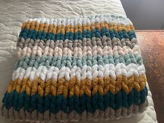 a crocheted blanket sitting on top of a bed next to a wooden floor